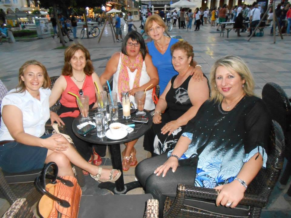 Έξι γυναίκες χαμογελούν καθισμένες σε τραπέζι καφετέριας σε εξωτε…