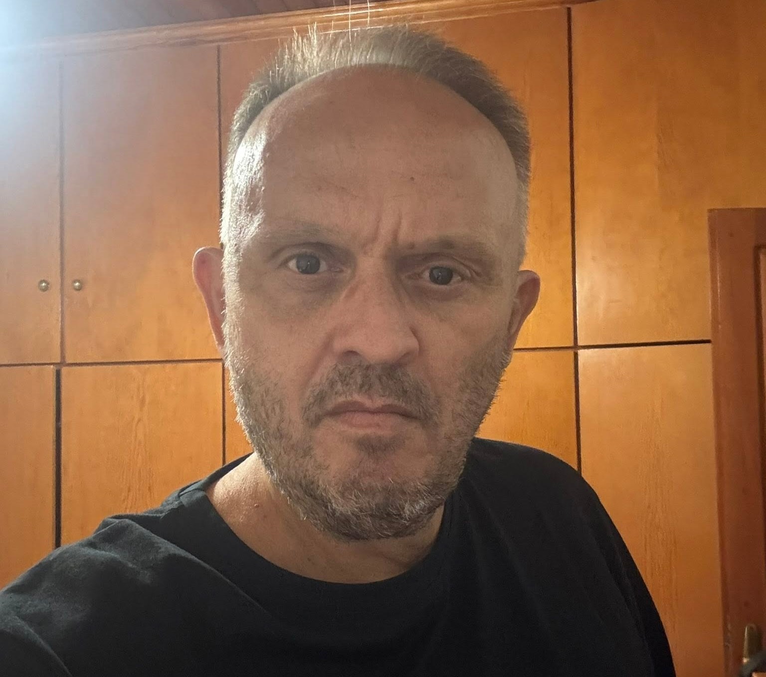 Άνδρας με γκρίζα μαλλιά και γένια, σοβαρό ύφος, φοράει μαύρο μπλουζ…
