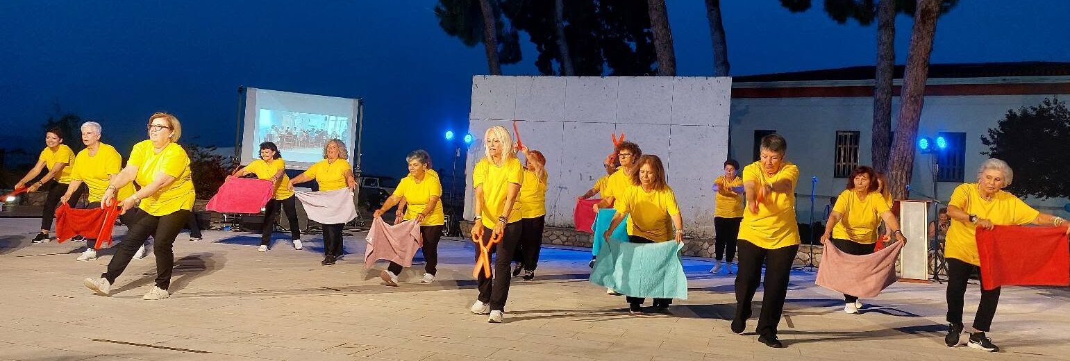 Γυναίκες από τα ΚΑΠΗ Αιγιαλείας με κίτρινες μπλούζες χορεύουν με π…