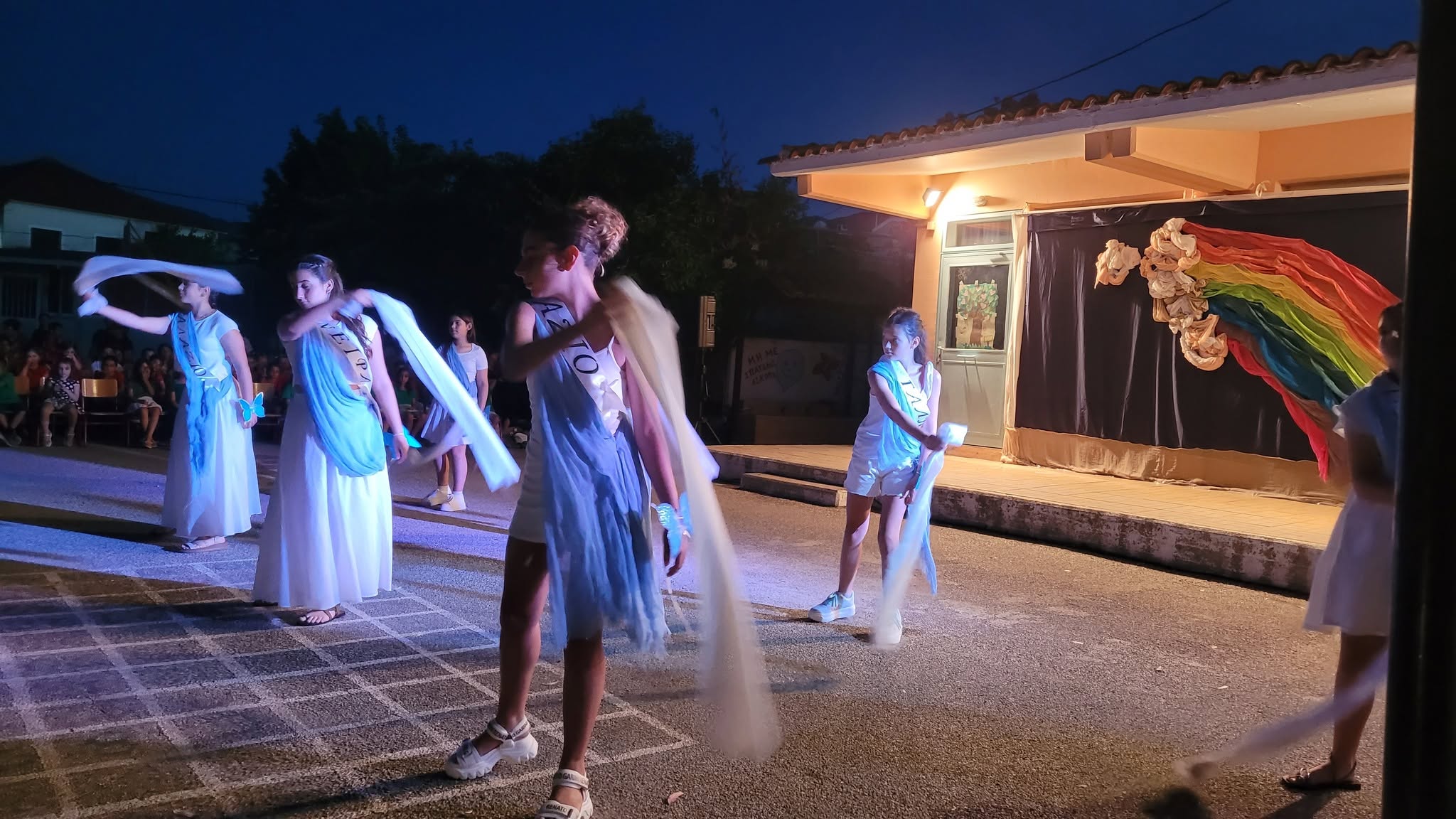 Μαθήτριες χορεύουν με λευκά ρούχα και υφάσματα σε σχολική γιορτή λ…
