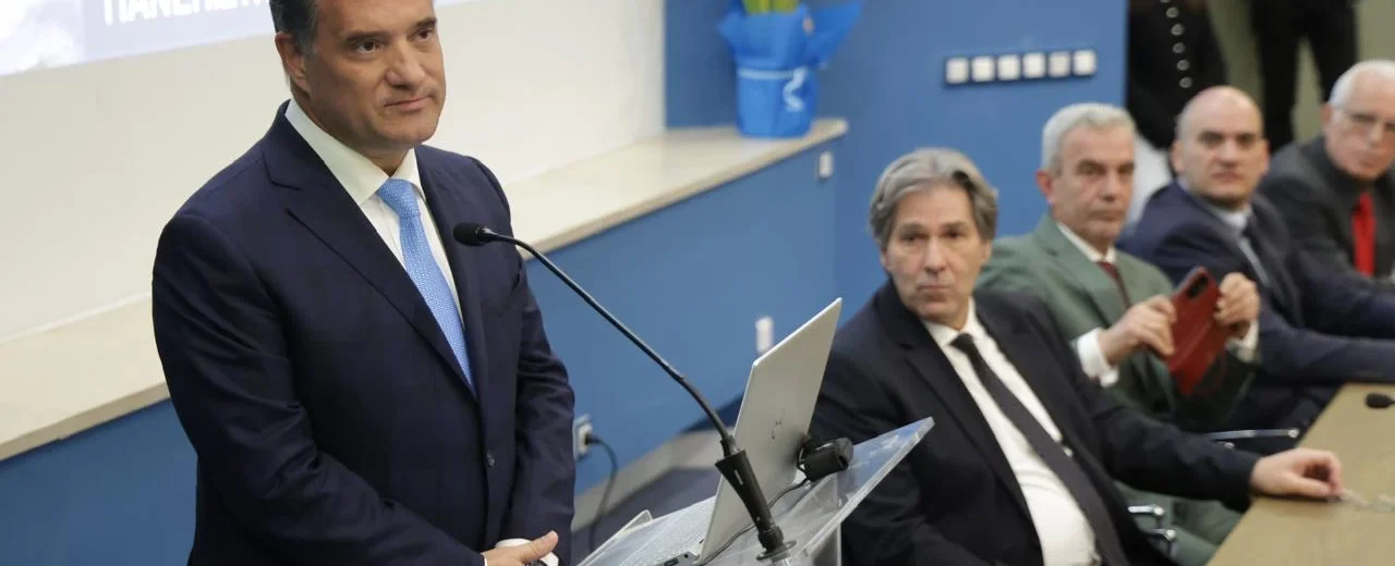 Ο Άδωνις Γεωργιάδης μιλάει από βήμα σε εκδήλωση στην Πάτρα, με άλλο…