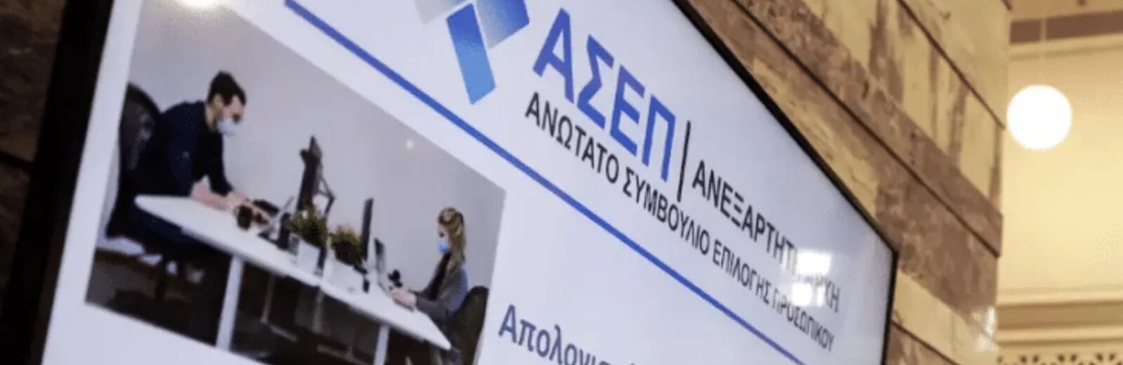 Οθόνη με το λογότυπο ΑΣΕΠ, εργαζόμενους και κείμενο για απολογισμό…