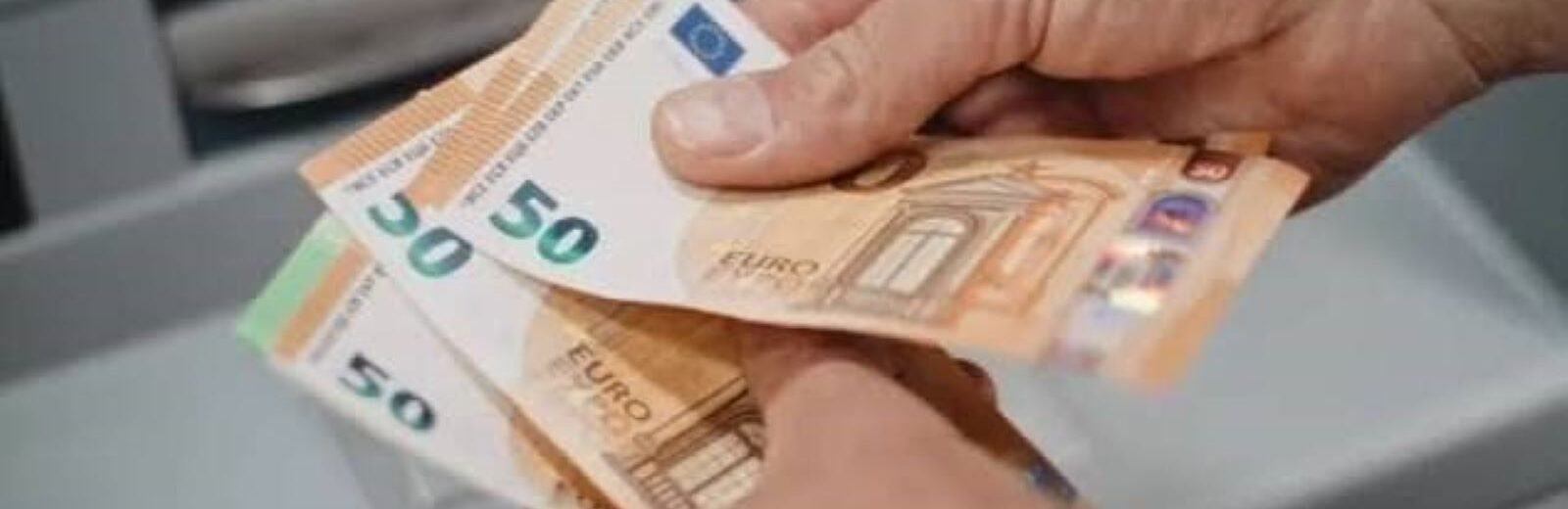 Χέρια κρατούν χαρτονομίσματα 50 ευρώ μπροστά σε ΑΤΜ.