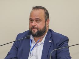 Ομιλητής με γενειάδα και μπλε σακάκι μιλά σε μικρόφωνα.