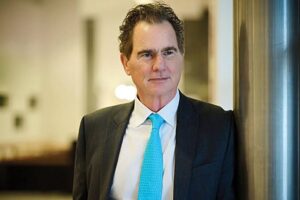 Πορτρέτο άνδρα με σκούρο κοστούμι, λευκό πουκάμισο και γαλάζια γρα…