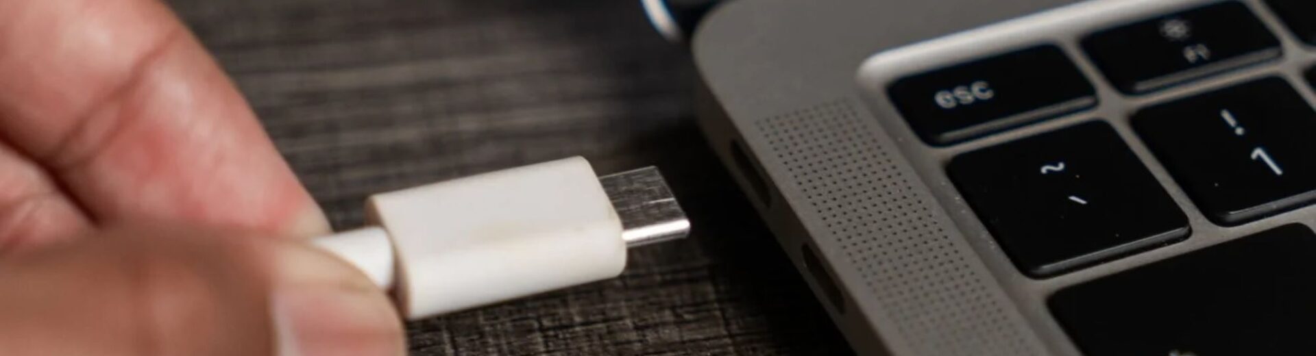 Χέρι συνδέει λευκό καλώδιο USB-C σε θύρα φορητού υπολογιστή.