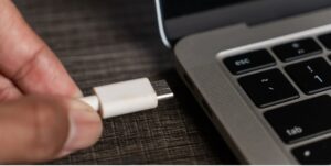 Χέρι συνδέει λευκό καλώδιο USB-C σε θύρα φορητού υπολογιστή.