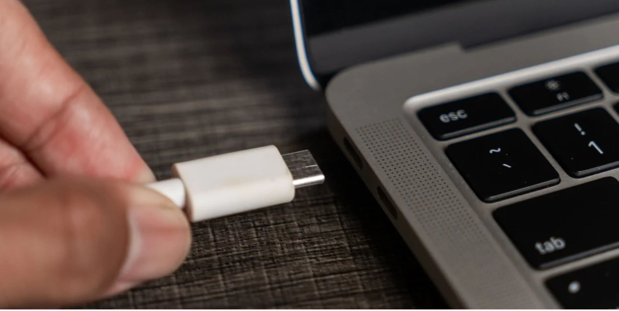 Χέρι συνδέει λευκό καλώδιο USB-C σε θύρα φορητού υπολογιστή.