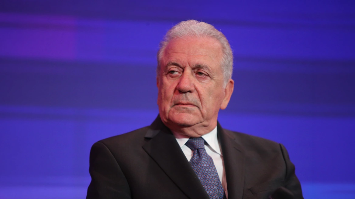 Ο Δημήτρης Αβραμόπουλος με κοστούμι και γραβάτα, κοιτάζει με σοβαρ…