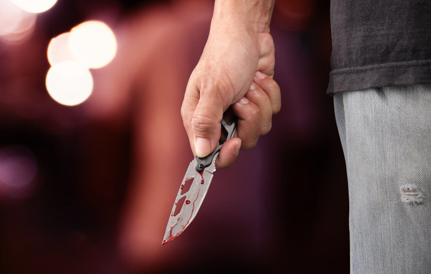 Ανθρώπινο χέρι κρατά μαχαίρι με αίμα στη λεπίδα, με θολό φόντο.
