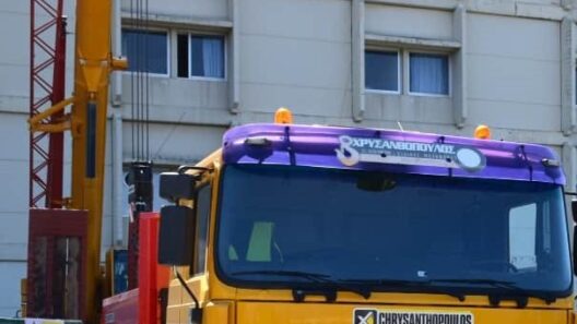 Κίτρινο γερανοφόρο όχημα με λογότυπο ΧΡΥΣΑΝΘΟΠΟΥΛΟΣ μπροστά σε κτ…