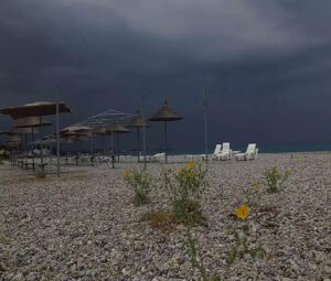 Μια βοτσαλωτή παραλία με ψάθινες ομπρέλες και ξαπλώστρες κάτω από …
