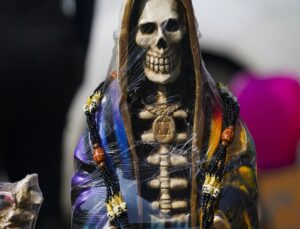 Κοντινό πλάνο αγάλματος σκελετού Santa Muerte τυλιγμένου σε πλαστικό, διακοσμημένο με μενταγιόν Άστρο του Δαβίδ και χάντρε…