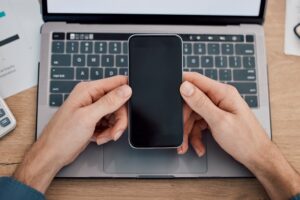 Κινητό τηλέφωνο στα χέρια πάνω από laptop, σύμβολο για το νέο voucher κινη…