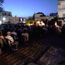 Κοινό παρακολουθεί μουσική εκδήλωση σε εξωτερικό χώρο το βράδυ, με…