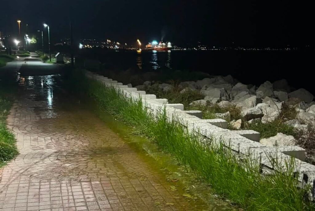 Νυχτερινή άποψη παραλιακού πεζόδρομου με λιμνάζοντα νερά, αντανακ…