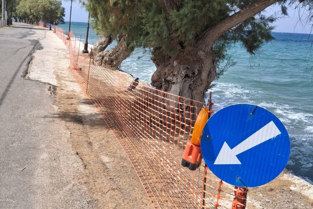 Διαβρωμένος παραλιακός δρόμος με πορτοκαλί δίχτυ ασφαλείας και μπ…