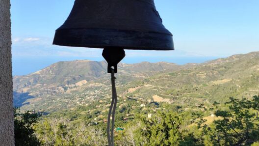 Καμπάνα εκκλησίας με θέα σε καταπράσινα βουνά, ένα χωριό και τη θάλ…
