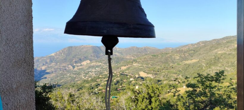 Καμπάνα εκκλησίας με θέα σε καταπράσινα βουνά, ένα χωριό και τη θάλ…