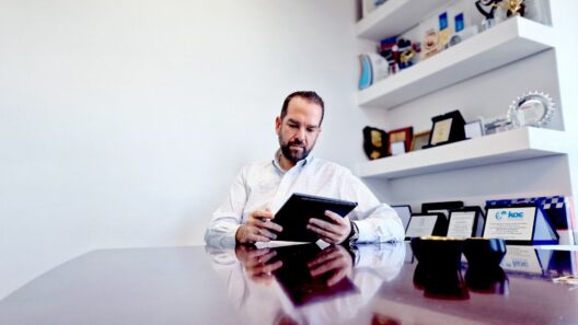 Αχαΐα: Χρηματοδότηση για την Προσχολική Εκπαίδευση και τη Δημιουργική Απασχόληση Παιδιών 12 Γενειοφόρος άνδρας με γυαλιά κοιτάζει μια ταμπλέτα σε γραφείο με β…
