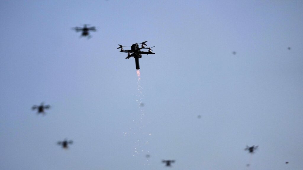 Ένα drone εκτοξεύει φλόγες και σπίθες στον ουρανό, με άλλα drones στο βάθ…