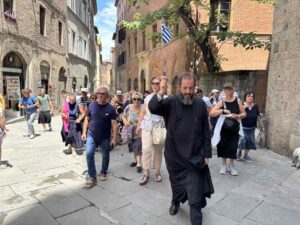 Ιερέας με ελληνική σημαία οδηγεί ομάδα ενοριτών σε στενό δρόμο στη…