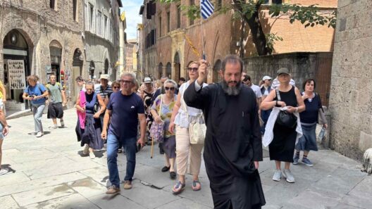 Ιερέας με ελληνική σημαία οδηγεί ομάδα ενοριτών σε στενό δρόμο στη…