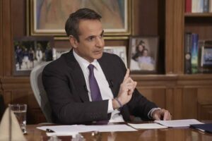 Ο Κυριάκος Μητσοτάκης σε γραφείο, φορώντας κοστούμι, με το δεξί χέρ…