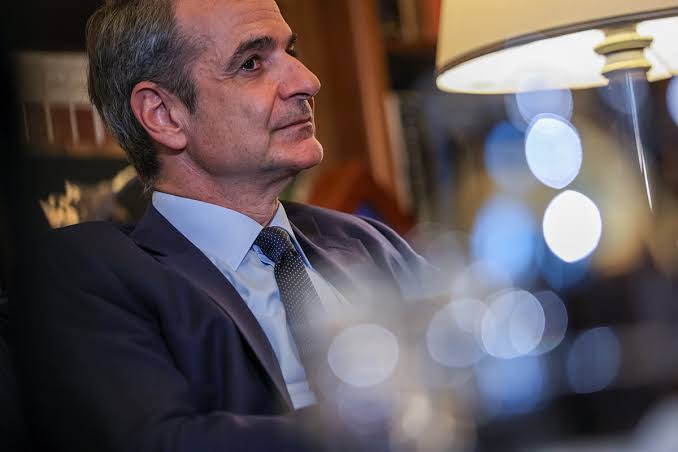 Ο Κυριάκος Μητσοτάκης με κοστούμι και γραβάτα, κοιτάζει δεξιά, με θ…