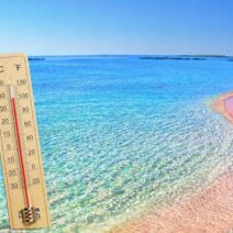 Θερμόμετρο σε παραλία με ροζ άμμο και γαλάζια νερά, δείχνει υψηλή θ…