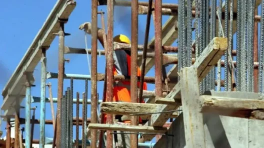 Εργάτης σε εργοτάξιο με σκαλωσιές και οπλισμό σκυροδέματος.