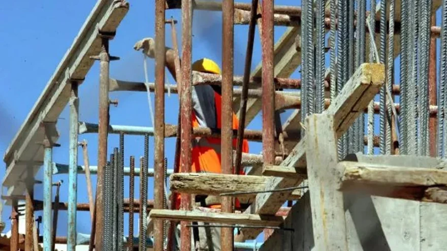Εργάτης σε εργοτάξιο με σκαλωσιές και οπλισμό σκυροδέματος.