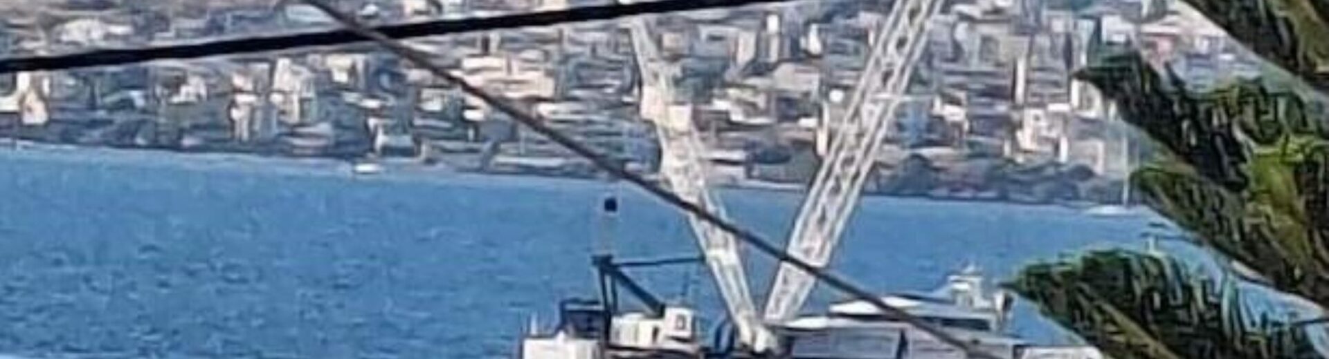 Πλωτός γερανός στη θάλασσα της Σαλαμίνας, με κτίρια και λόφους στο …