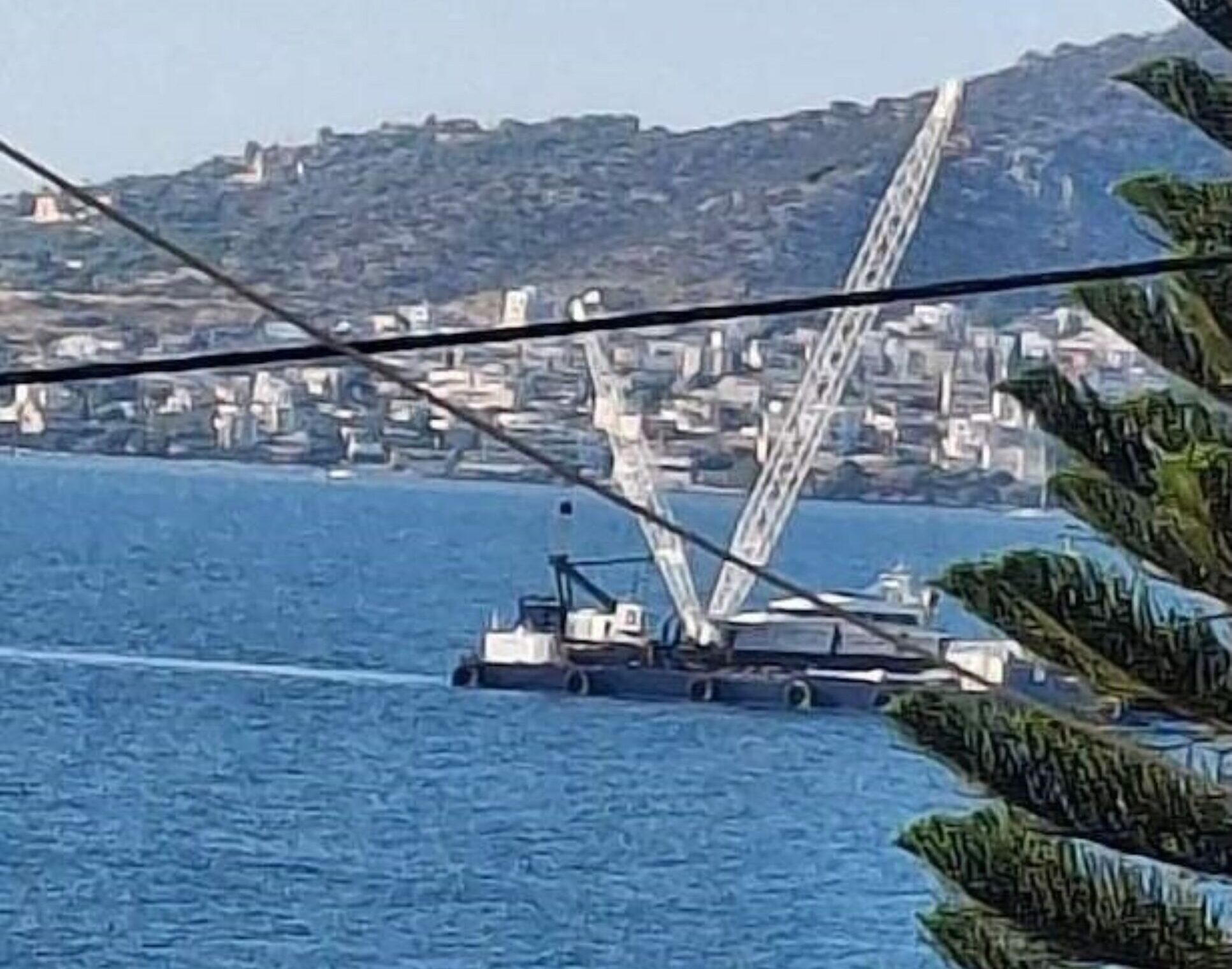 Πλωτός γερανός στη θάλασσα της Σαλαμίνας, με κτίρια και λόφους στο …