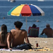 Ένα ζευγάρι κάθεται σε αμμώδη παραλία, κοιτάζοντας τη θάλασσα κάτω…