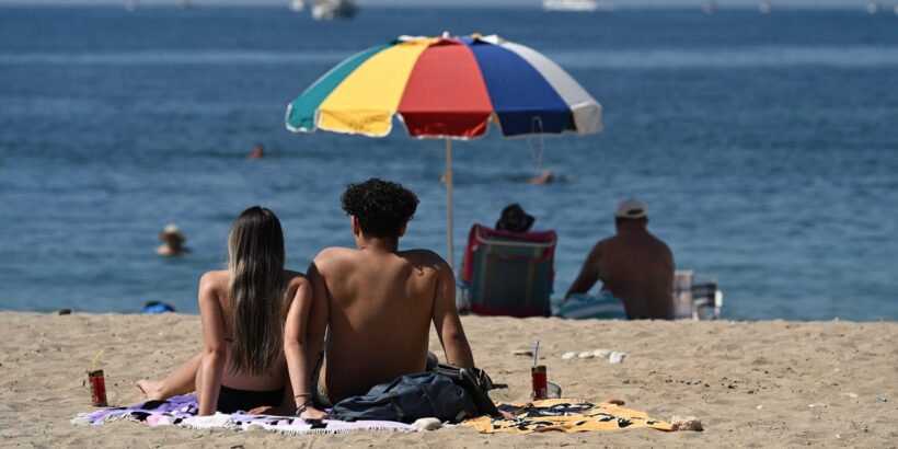 Αχαΐα: Καύσωνας προ των πυλών στην περιοχή για πρώτη φορά 4 Ένα ζευγάρι κάθεται σε αμμώδη παραλία, κοιτάζοντας τη θάλασσα κάτω…