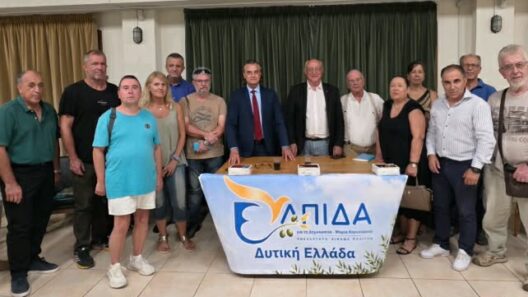 Μια ομάδα ανθρώπων, συμπεριλαμβανομένου ενός άνδρα με κοστούμι, στέκονται πίσω από ένα τραπέζι με το πανό «ΕΛΠΙΔΑ Δυτική Ε…
