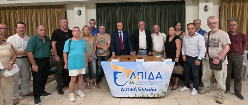 Πάτρα: Εστησε κομματικό μηχανισμό η «Ελπίδα» της Καρυστιανού για μια νέα αρχή και κατέρχεται στην Αχαΐα 4 Μια ομάδα ανθρώπων, συμπεριλαμβανομένου ενός άνδρα με κοστούμι, στέκονται πίσω από ένα τραπέζι με το πανό «ΕΛΠΙΔΑ Δυτική Ε…