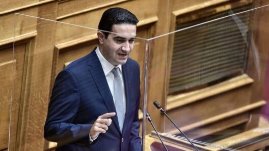 Πολιτικός μιλάει σε βήμα στη Βουλή, πίσω από προστατευτικό πλεξιγκ…