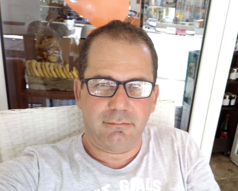 Ένας άνδρας με γυαλιά και γκρι μπλουζάκι κοιτάζει την κάμερα, με ψη…