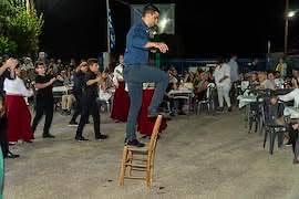 Άνδρας χορεύει πάνω σε καρέκλα σε παραδοσιακό γλέντι με πλήθος κόσ…