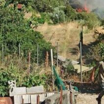 Άνδρας περπατά με φωτιά και καπνό σε λόφο στο βάθος.