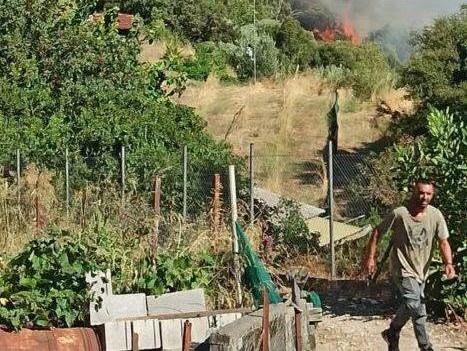Άνδρας περπατά με φωτιά και καπνό σε λόφο στο βάθος.