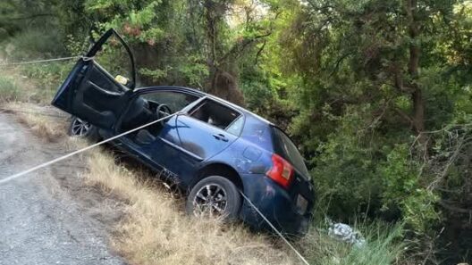 Μπλε αυτοκίνητο κρέμεται με σχοινιά στην άκρη ενός χωματόδρομου, έ…