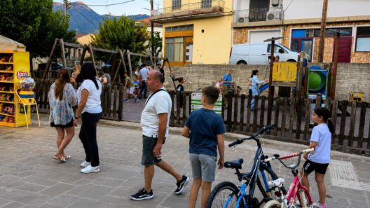 Κλειτορία: Με «οσμή σκανδάλου» μαίνεται ο θόρυβος για πώληση οικοπέδου Παιδικής χαράς σε ιδιώτη 13 Άνθρωποι περπατούν σε πλακόστρωτο δίπλα σε ξύλινη παιδική χαρά όπου παίζουν παιδιά. Δύο παιδιά στέκονται με ποδήλατα στο π…