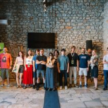 AISFF5 | «Φωτίζοντας τον διάλογο» στο Αίγιο 1 Ομάδα ανθρώπων και ένα σκυλάκι ποζάρουν μπροστά σε πέτρινο τοίχο σ…