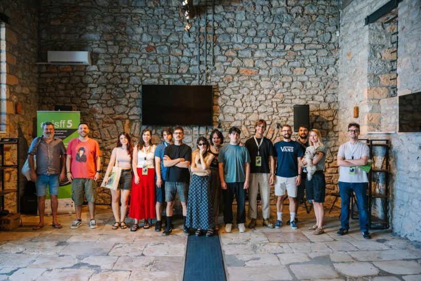 AISFF5 | «Φωτίζοντας τον διάλογο» στο Αίγιο 4 Ομάδα ανθρώπων και ένα σκυλάκι ποζάρουν μπροστά σε πέτρινο τοίχο σ…