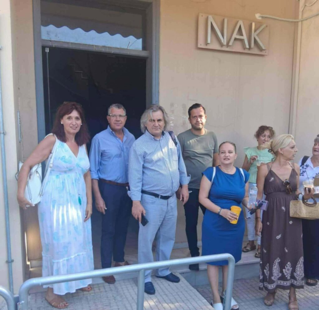 Ομάδα ανδρών και γυναικών στέκεται έξω από κτίριο με την πινακίδα I…