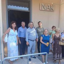 Ομάδα ανδρών και γυναικών στέκεται έξω από κτίριο με την πινακίδα I…