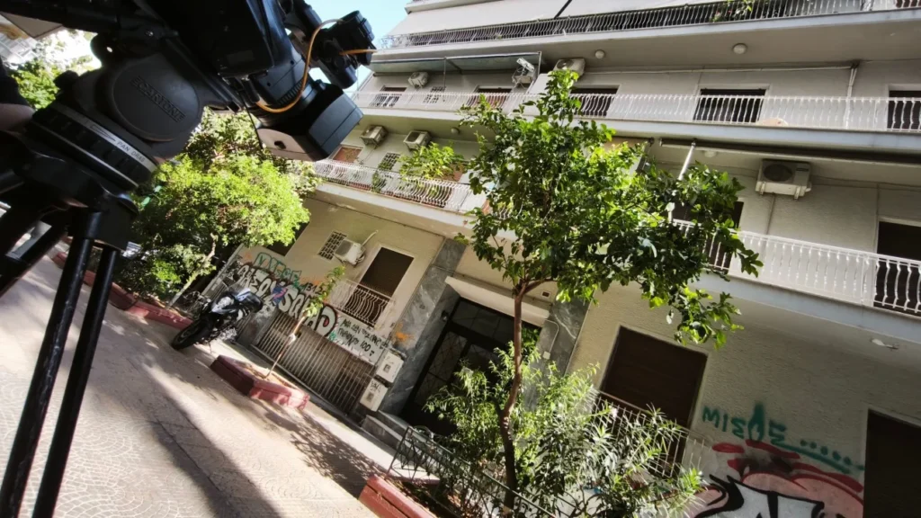 Κάμερα σε τρίποδο μπροστά σε πολυκατοικία στην Κυψέλη, με γκράφιτι…